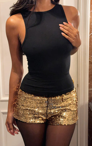 model wears black tank top and gold sequin mini shorts with black stockings.